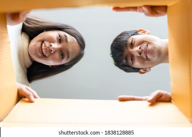 Smiling Asian Young Couple Opening Cardboard Box Or Parcel And Looking Inside