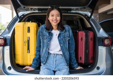 Smiling Asian young girl sit on suv car trunk with suitcases or luggages. She ready to go road trip with her friends. - Shutterstock ID 2203206593