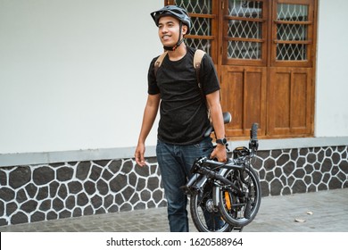 smiling asian young man carrying her folding bike before go in front the house - Powered by Shutterstock