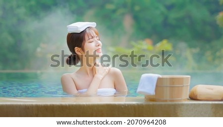 smiling asian young woman sitting on the bathtub is relaxing in hot spring with towel on head