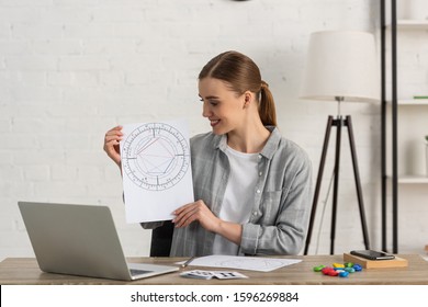 Smiling Astrologer Holding Natal Chart With Cards With Zodiac Signs On Table