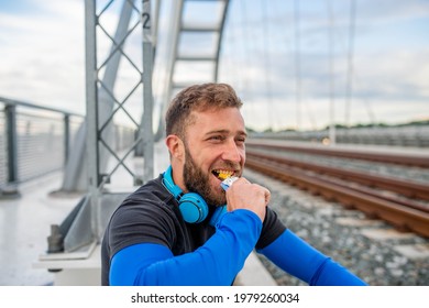 A Smiling Athlete With A Beard Eating A Bar Of Chocolate After Training