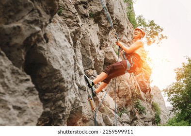 Smiling athletic woman in protective helmet and shoes climbing cliff rock wall using top rope and harness in Paklenica National park site in Croatia. Active extreme sports time spending concept - Powered by Shutterstock