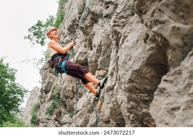 Smiling athletic woman in protective helmet and shoes climbing cliff rock wall using top rope and harness in Paklenica National park site in Croatia. Active extreme sports time spending concept - Powered by Shutterstock