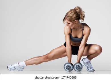 Smiling athletic woman pumping up muscles with dumbbells and stretching legs