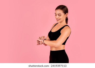 Smiling athletic woman in sportswear checking her smartwatch, beautiful young female looking at fitness tracker during workout session, posing isolated against pink studio background, copy space - Powered by Shutterstock