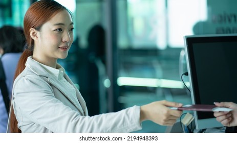 Smiling Attendant Working At Check-in Desk In Airport. Female Airline Staff Checking Passport Of Traveler..