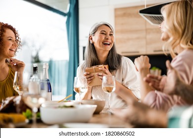 Smiling attractive Asian woman holding gift box while laughing at home - Powered by Shutterstock