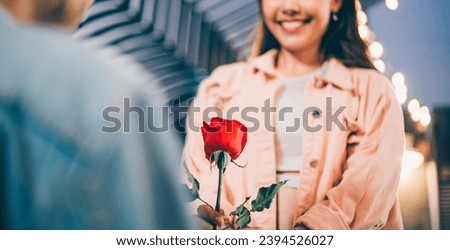 Smiling attractive Asian woman looks happy and surprise receiving rose flower from her boyfriend for Valentine's day or proposal. love and togetherness concept