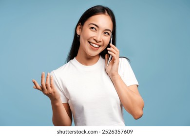 Smiling, attractive Asian woman talking, answering call on phone and gesturing with hand isolated on blue background. Communication concept - Powered by Shutterstock