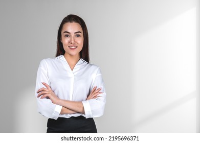 Smiling attractive businesswoman wearing formal wear is standing crossed arms near empty white wall in background. Concept of model, successful business person, student, confidence - Shutterstock ID 2195696371
