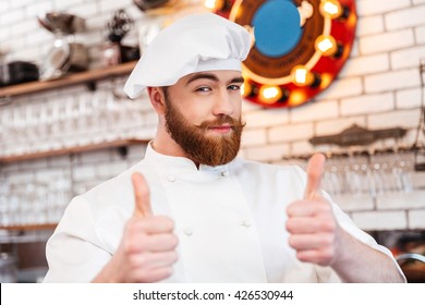 Smiling attractive chef cook showing thumbs up on the kitchen - Powered by Shutterstock