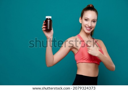 Smiling attractive female wearing sport fit holding a bottle with pills or drugs and show finger to product ad 商業照片 © 