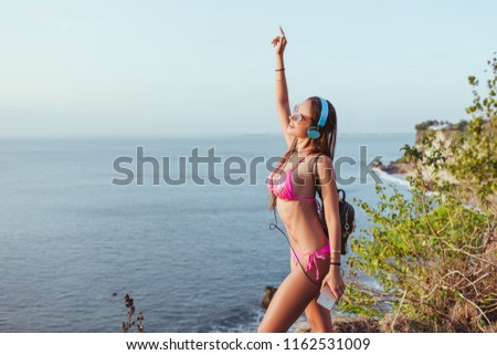 smiling attractive girl in headphones and pink bikini dancing at beach