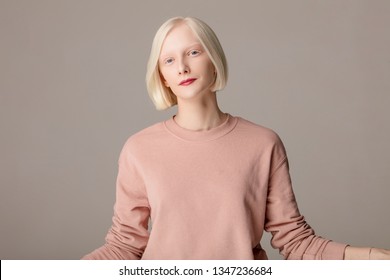 smiling attractive girl in pink stylish sweater isolated on the grey background, close up photo.