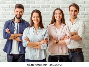 Smiling Attractive Group Of Young People Standing With Crossed Arms, Against A Background Of A Brick Wall