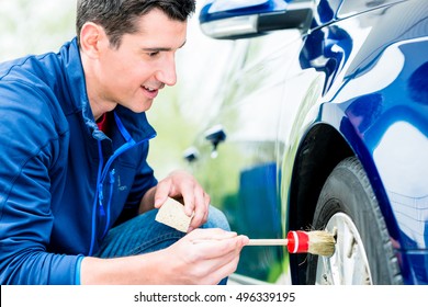 Smiling Attractive Man Cleaning The Alloy Hubs On His Car Tyres Using A Soft Bristle Brush And Soap