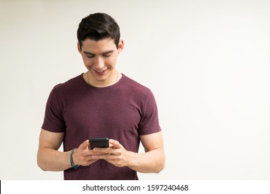 Smiling Attractive Man Using Mobile Phone While Standing Against Plain Background