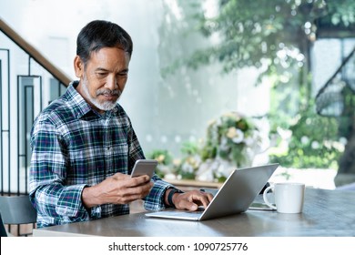 Smiling Attractive Mature Man With White, Grey Stylish Short Beard Using Smartphone Gadget Serving Internet In Modern Office,co-working Space Or Coffee Shop. Old Man Using Social Network Technology.