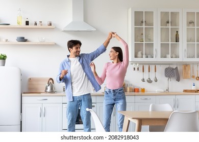 Smiling Attractive Millennial European Couple Have Fun Together, Feeling Happy, Dance In Kitchen Interior. Joy, Romantic Date, Celebration Anniversary And Positive Weekend At Home During Covid-19