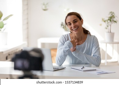 Smiling Attractive Mixed Race Woman Sitting At Table In Front Of Digital Camera, Recording Educational Lecture For Personal Channel In Social Network. Happy Young Lady Filming Self Presentation.