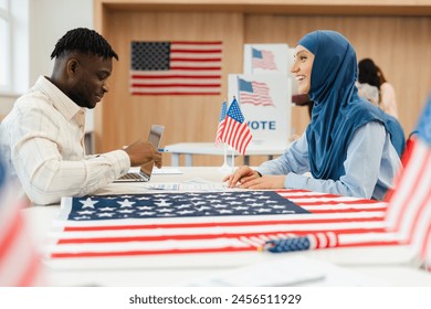 Smiling, attractive Muslim woman wearing hijab waiting in line voters registration at polling station. Democracy, vote, US presidential election concept - Powered by Shutterstock