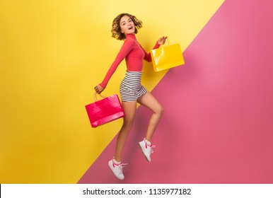 Smiling Attractive Woman In Stylish Colorful Outfit Jumping With Shopping Bags, Happy, Pink Yellow Background, Polo Neck, Striped Mini Skirt, Sale, Discount, Shopaholic, Fashion Summer Trend, Emotiona