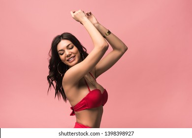 smiling attractive woman in swimsuit dancing isolated on pink