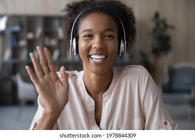 Smiling Attractive Young African American Woman In Headphones Looking At Camera, Waving Hands, Starting Online Video Call Zoom Conversation, Enjoying Pleasant Remote Talk, Distant Communication.