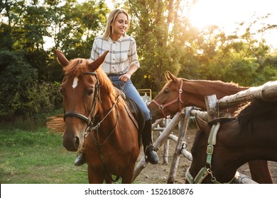 Smiling attractive young blonde girl riding a horse at the horse yard