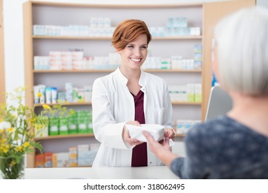 Smiling attractive young redhead pharmacist handing over prescribed medicines to an elderly female patient, view over the clients shoulder of the pharmacist - Powered by Shutterstock