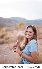 Smiling and attractive young woman drinking traditional Argentinian yerba mate tea from a calabash gourd with bombilla stick on a sunny day in the mountain.