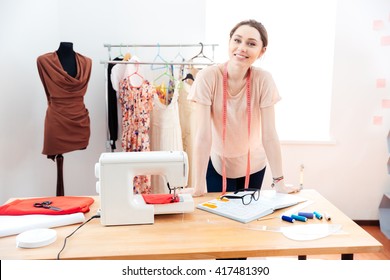 Smiling attractive young woman fashion designer standing and working in studio