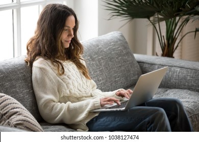 Smiling Attractive Young Woman Sitting On Sofa Using Laptop Communicating Working Online At Home, Happy Teen Girl Typing On Computer, Enjoying Writing Blog Or Chatting With Friends In Social Network