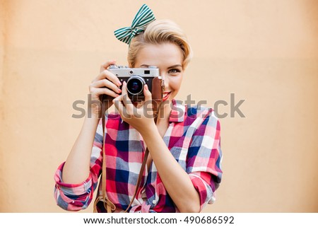 Smiling attractive young woman taking photos using old camera over pink background