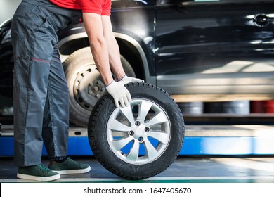 smiling auto mechanic carrying tire in tire store - Powered by Shutterstock