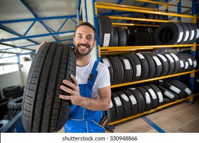 smiling auto mechanic carrying tire in tire store - Powered by Shutterstock