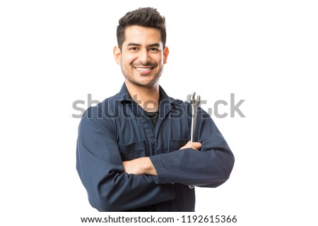 Smiling auto mechanic with wrench standing hands folded on white background