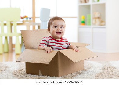 Smiling baby boy sitting inside cardboard box after moving to a new apartment