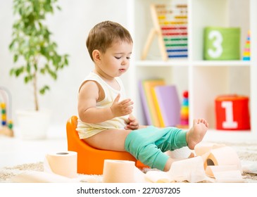 smiling baby sitting on chamber pot with toilet paper rolls
