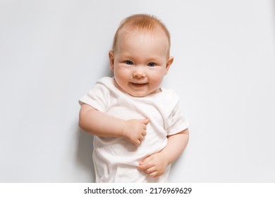 Smiling Baby (six Months) In White Clothes Looks In Camera, Emotive Portrait Of Child. Solid Background. Top View.