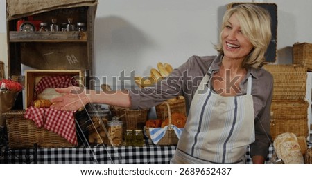Smiling baker in apron presenting baskets of breads and jars on table at stall, copy space. Artisan, bakery, foodstyling, rustic, hospitality, handcrafted, culinary