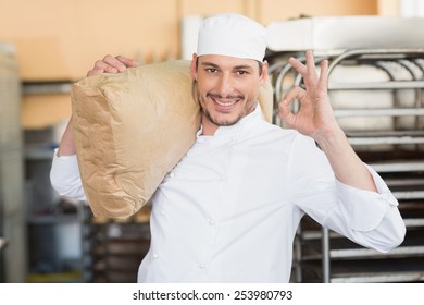 Smiling Baker Holding Bag Of Flour In The Kitchen Of The Bakery