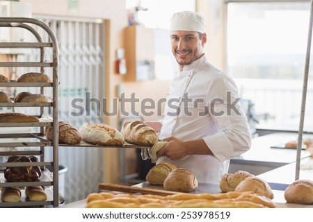 Smiling baker holding tray of bread in the kitchen of the bakery
