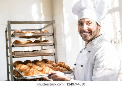 Smiling baker holding tray with fresh cooked croissants in bakehouse - Powered by Shutterstock