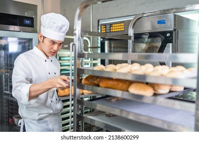 Smiling bakers looking at camera..Chef  baker in a chef dress and hat, cooking together in kitchen.Young asian man takes fresh baked cookies out of modern electric oven in kitchen. - Powered by Shutterstock