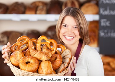 Smiling bakery assistant holding up a collection of assorted freshly baked rolls on display in a wicker basket - Powered by Shutterstock