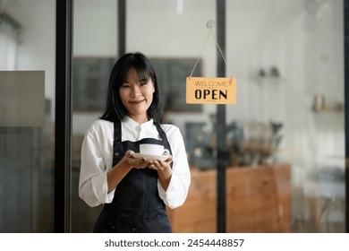 Smiling barista in apron holding a coffee cup with a welcoming open sign in the background at a cozy café.

 - Powered by Shutterstock