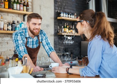 Smiling barista and young pretty woman in glasses talking in coffee shop