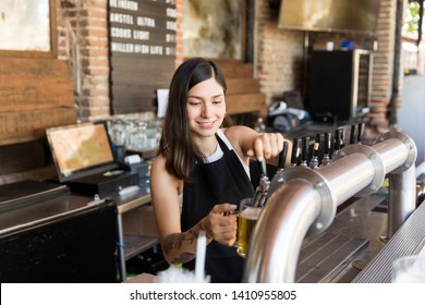 Smiling barmaid pouring beer from tap in glass at bar - Powered by Shutterstock